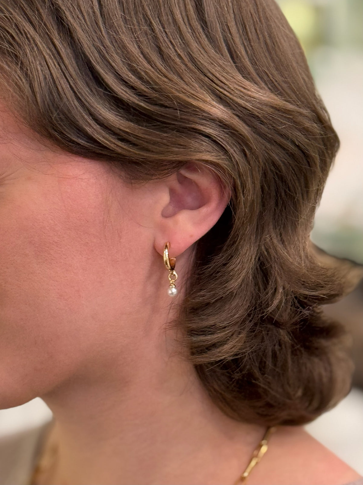 A pair of gold hoop earrings with a small white pearl dangle being worn