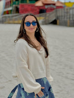 Ren Reversible Cropped Sweater in cream styled with aqua jewelry and blue sunglasses. On model at the beach