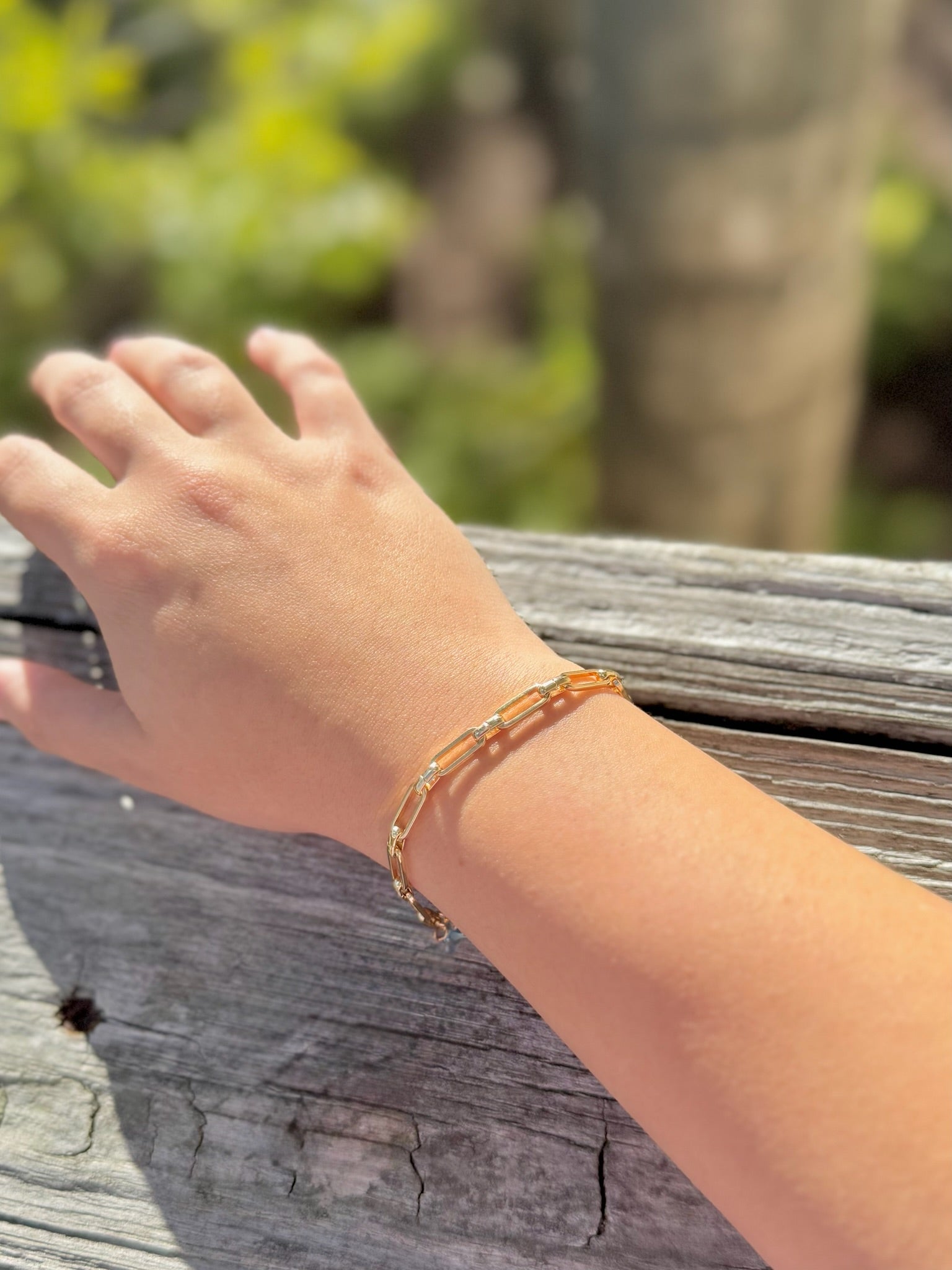 Hand wearing a bracelet on a wooden surface with a blurred natural background