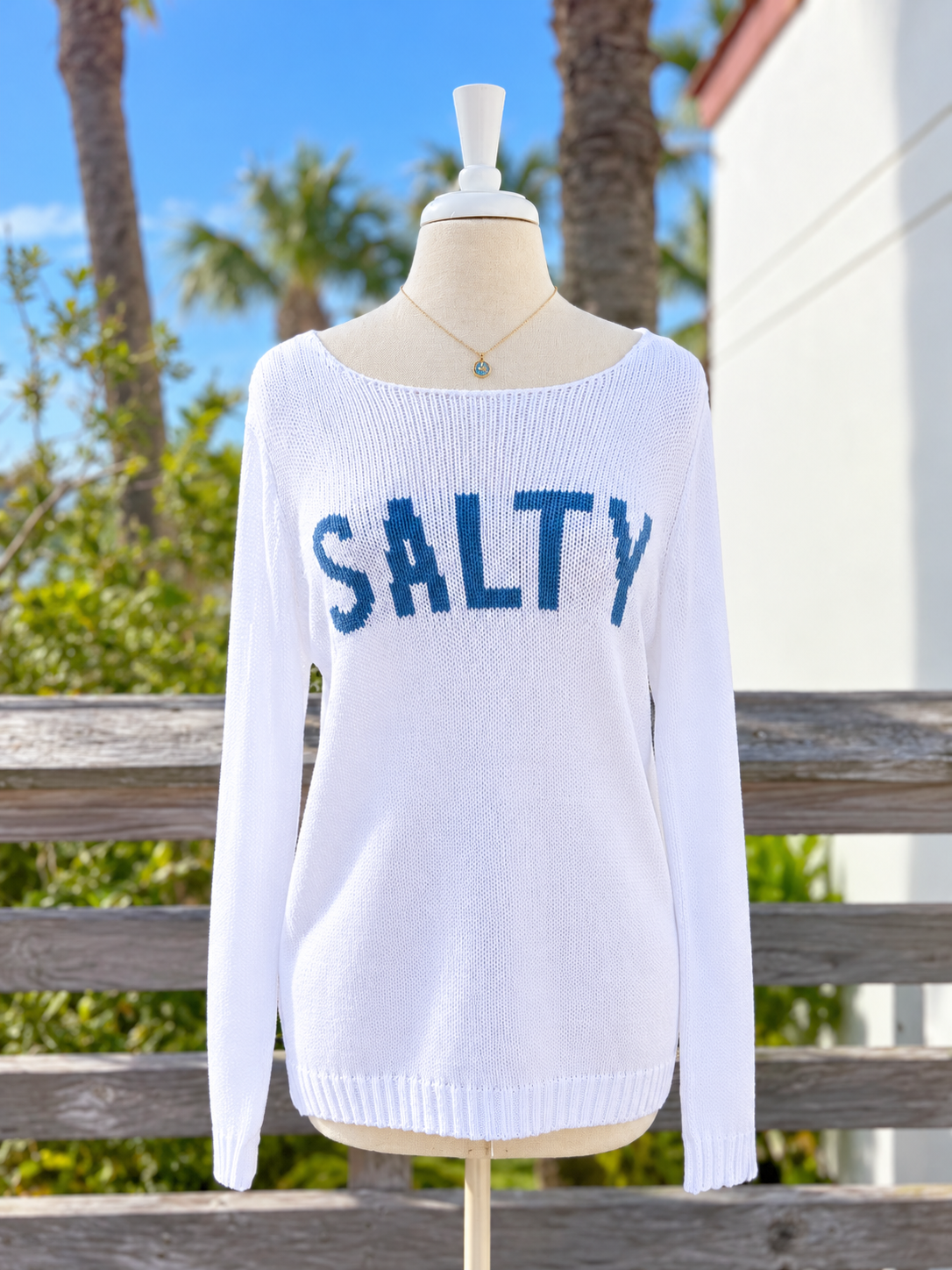 White lightweight knit SALTY sweater with blue lettering, wide boat neckline, relaxed fit, and long sleeves, photographed at Ardor Boutique.
