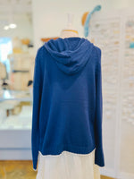 Back view of the Sarah Sweater in Navy Blue showing its relaxed hood, soft textured cotton-blend knit, long sleeves, ribbed cuffs, and white distressed hem trim.