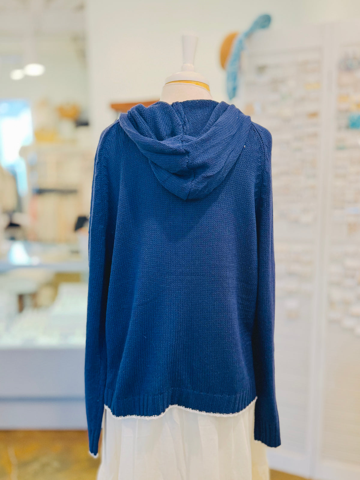 Back view of the Sarah Sweater in Navy Blue showing its relaxed hood, soft textured cotton-blend knit, long sleeves, ribbed cuffs, and white distressed hem trim.
