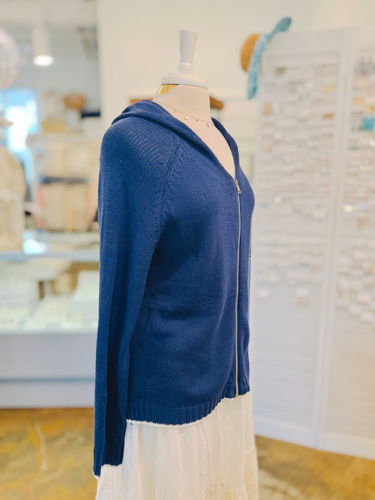 Side profile of the Sarah Sweater in Navy Blue showing the silver front zipper, hooded neckline, relaxed knit fit, long sleeves, and white hem edging.