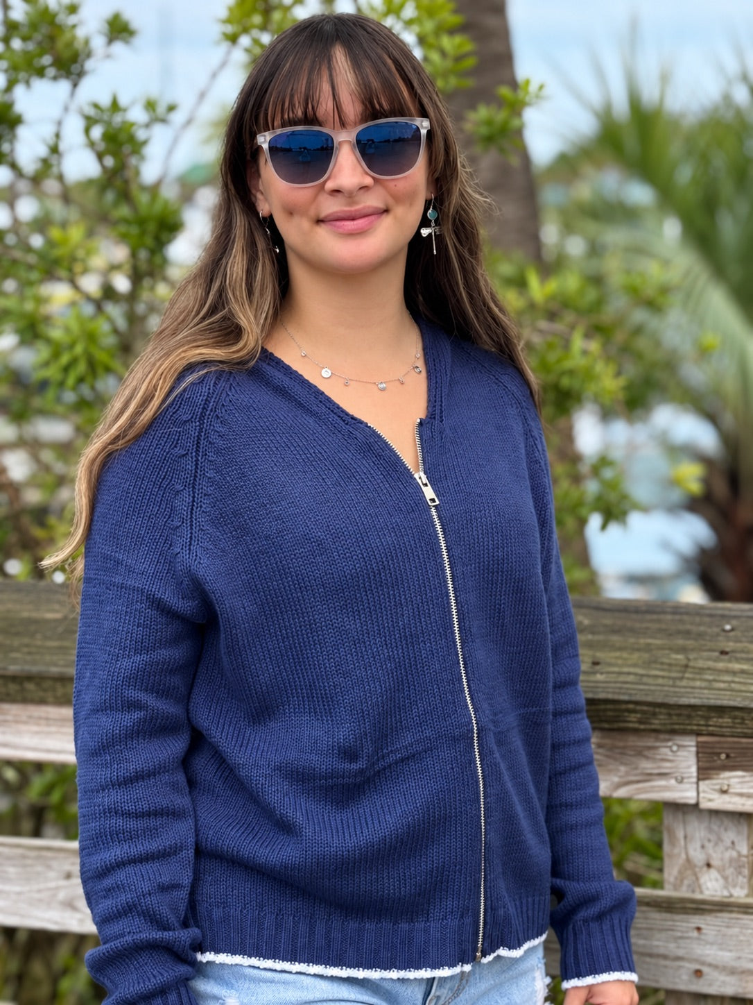 Woman wearing the Sarah Sweater in Navy, featuring a soft cotton-blend knit, full silver zipper, relaxed hood, long sleeves, and white trim along the hem and cuffs