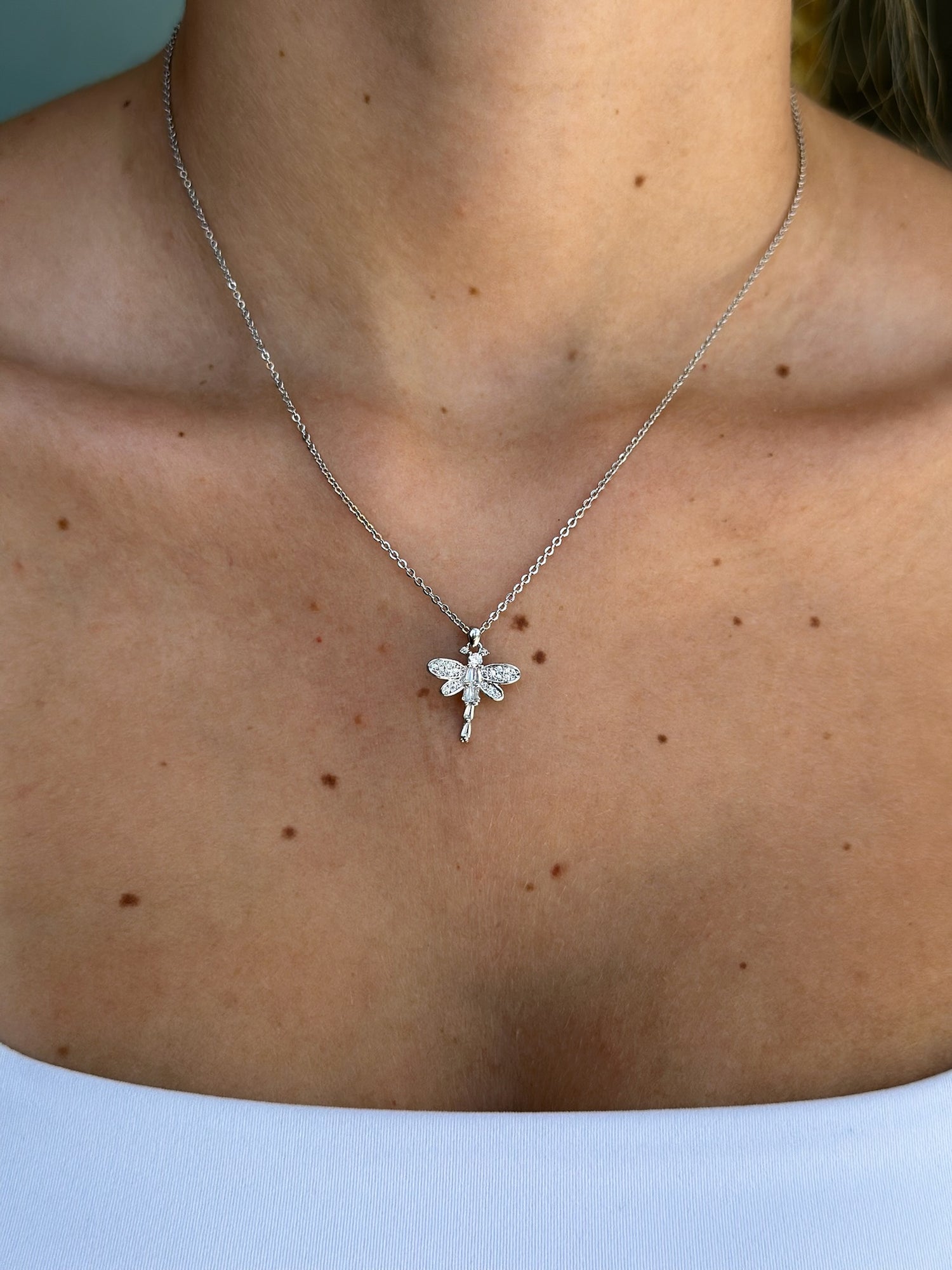 Silver necklace with a dragonfly pendant on a person's neck against a light background