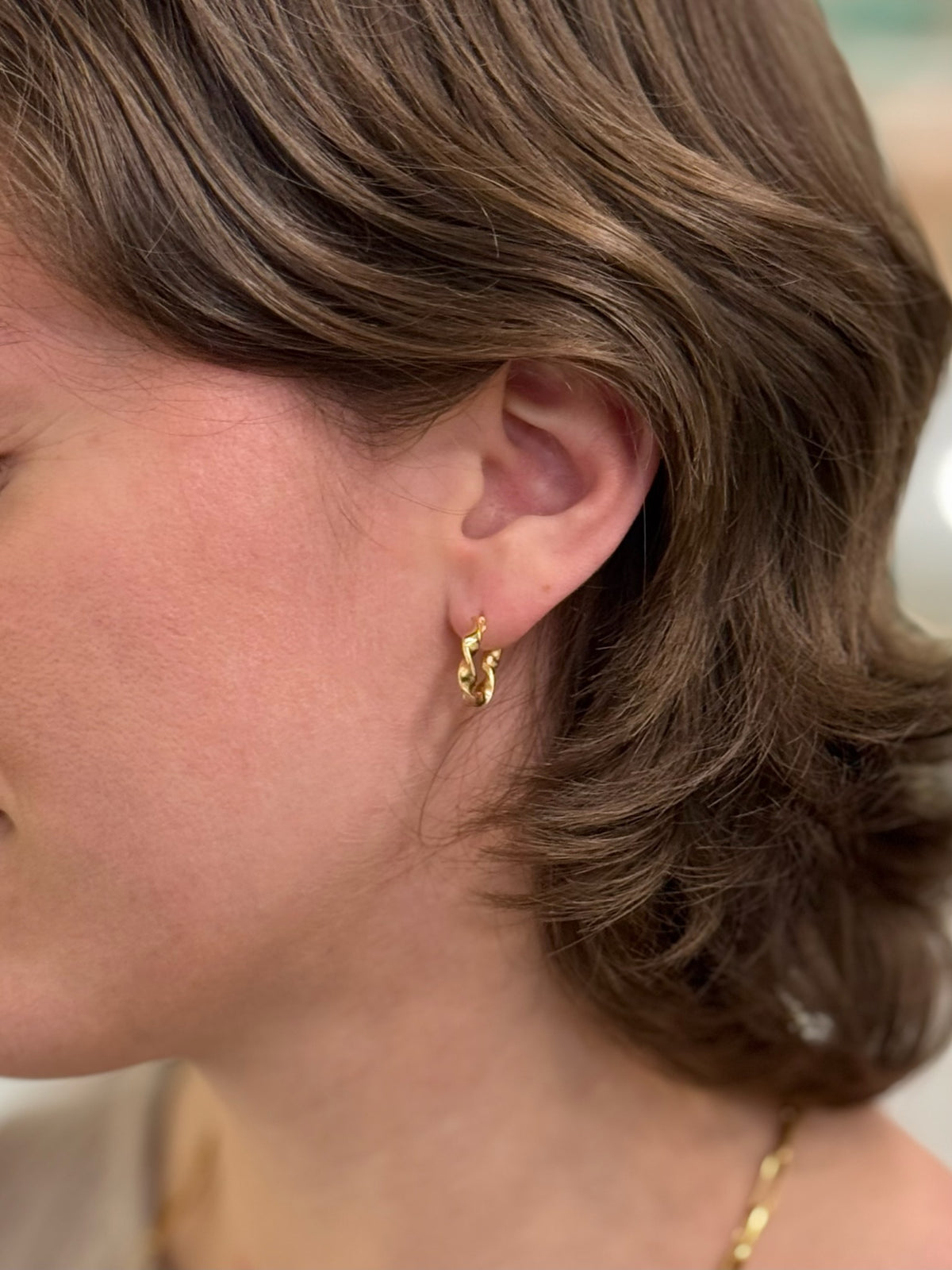 A pair of gold hoop earrings with a twisted, textured design being worn