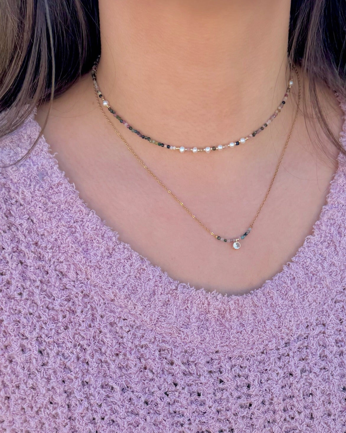 Close-up of a person wearing two necklaces with a pink textured top.