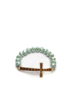 A bracelet with faceted green beads and a hammered gold-tone cross as its centerpiece, featuring an elastic design for a comfortable fit.