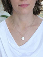Woman wearing the Veronica White Keshi Freshwater Pearl Necklace, featuring a large petal-shaped pearl on a sterling silver chain with a hammered rose gold loop and small pearl detail. Shown styled with a white draped neckline top.