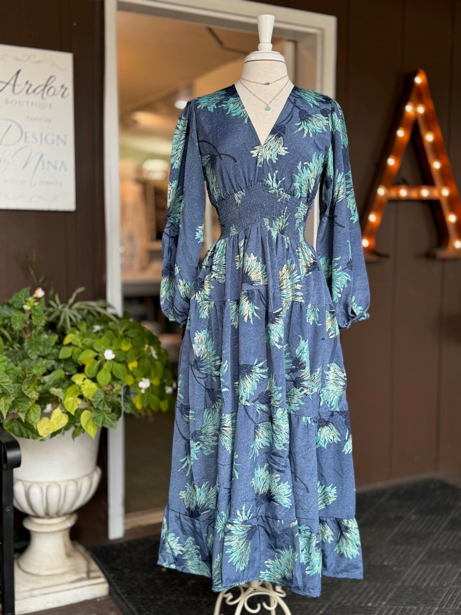 Blue maxi dress with aqua and gold floral print, v-neckline, smocked waistline, and elastic wrists displayed on mannequin