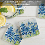 Set of four floral coasters with blue flowers on a white surface, accompanied by lemon slices and straws.