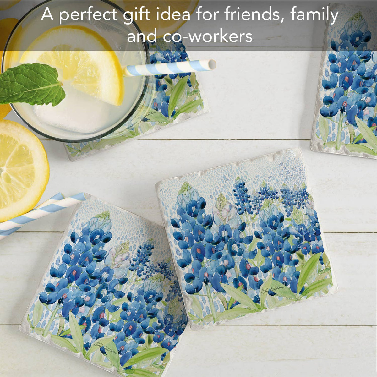 Set of four floral coasters with blue flowers on a white surface, accompanied by lemon slices and straws.