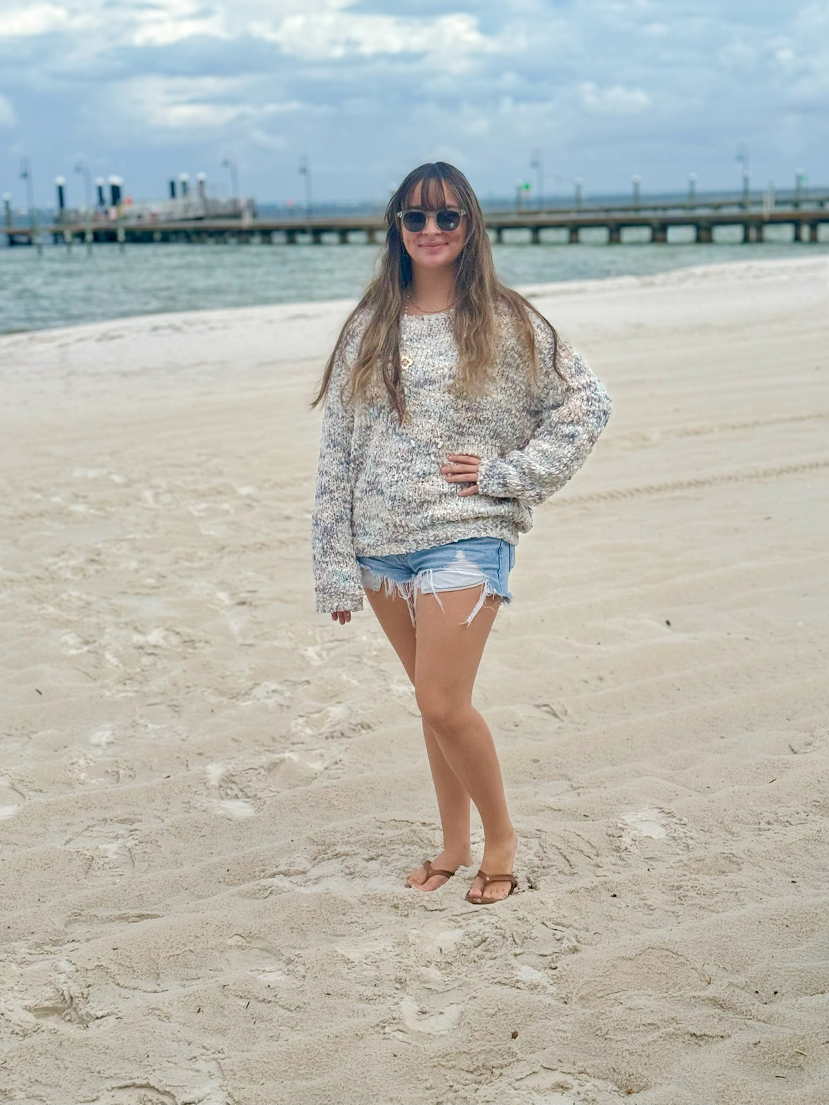 Front view of the Annie oversized blue-grey knit sweater worn with denim shorts on the beach.