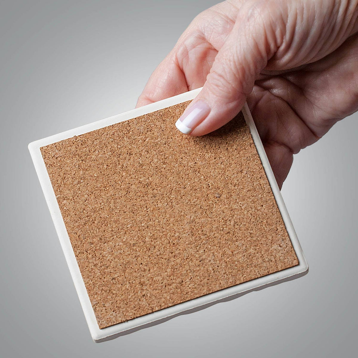 Square cork coaster held by a hand against a gray background