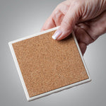 Square cork coaster held by a hand against a gray background