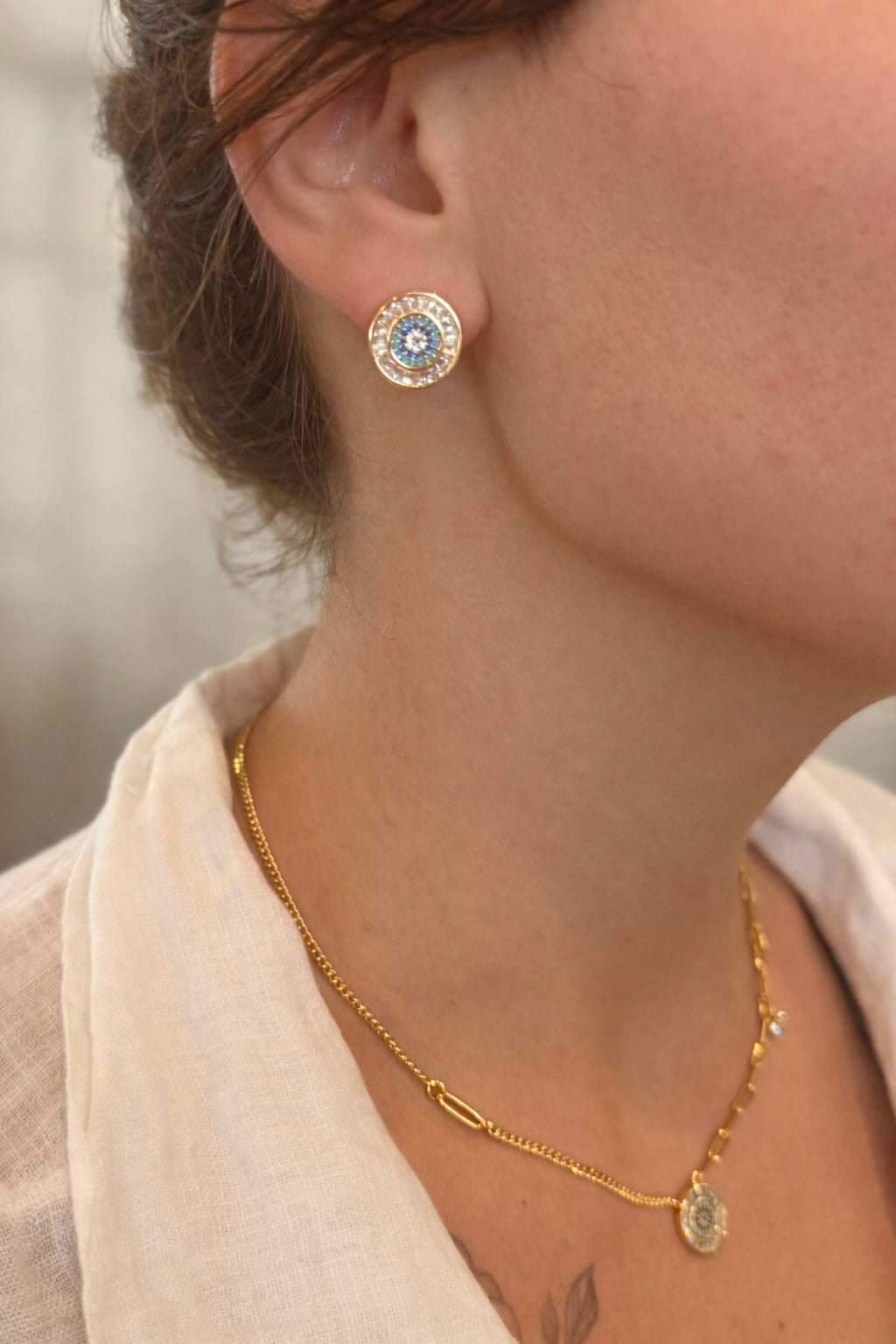 Close-up of a person wearing gold earrings and a gold necklace with a blurred background
