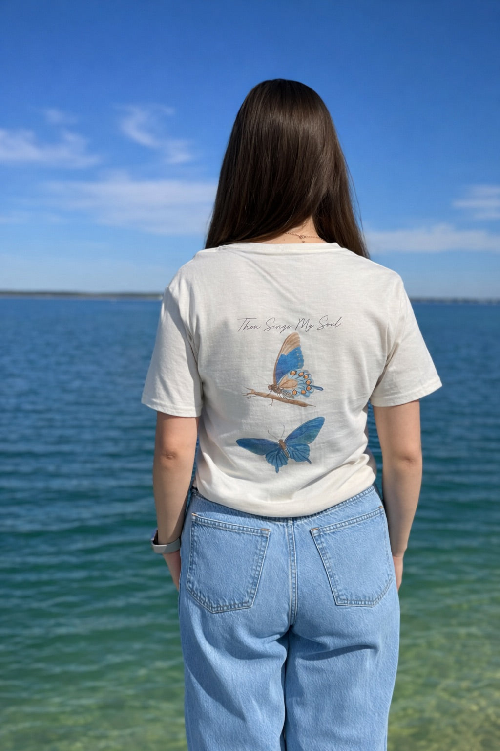 Person wearing a t-shirt with butterfly designs by the water