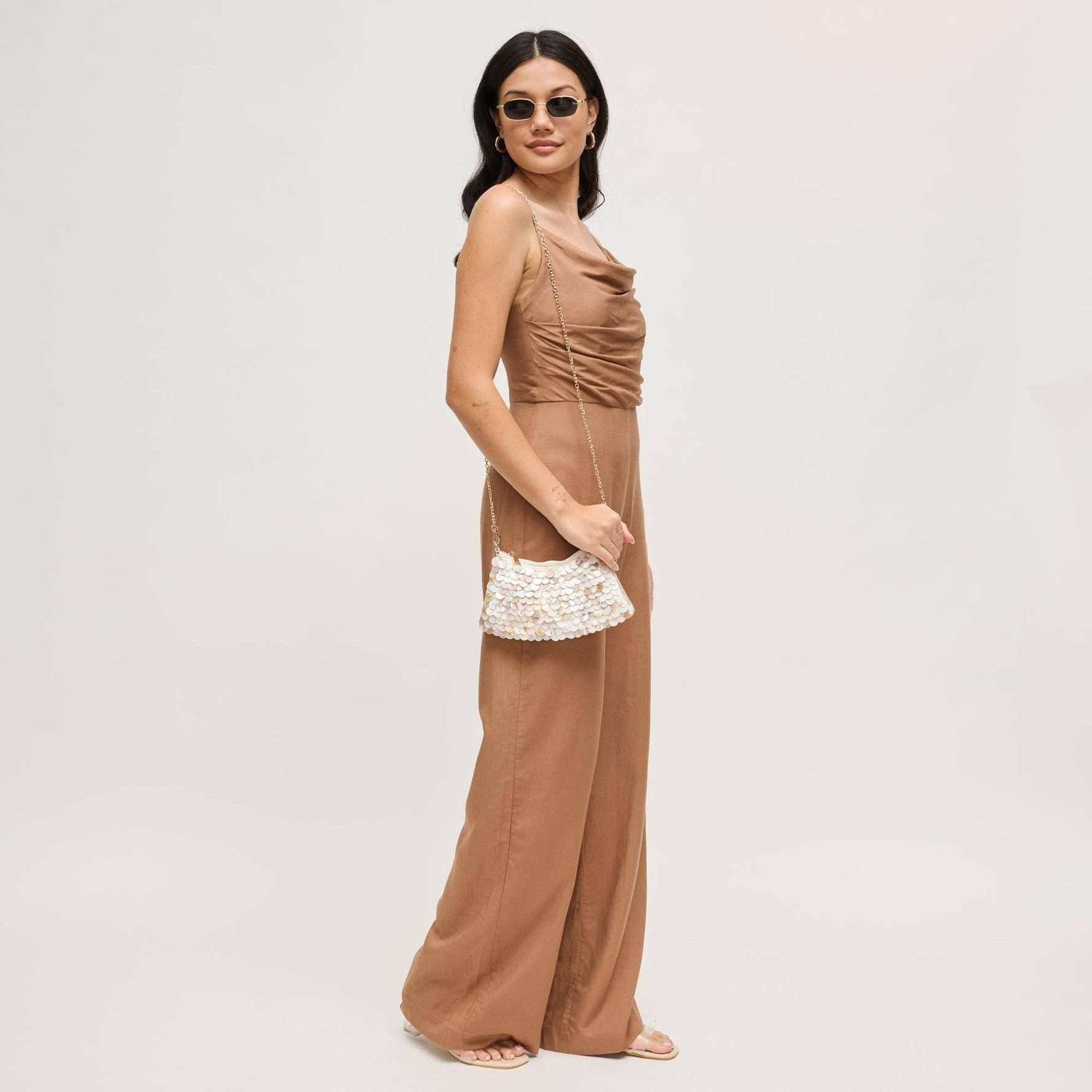 Model wearing the Opalite Evening Bag as a crossbody with a removable gold-tone chain strap, showcasing its shimmering opalescent shell disc embellishments.
