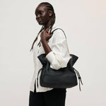 Woman holding a black handbag against a plain background