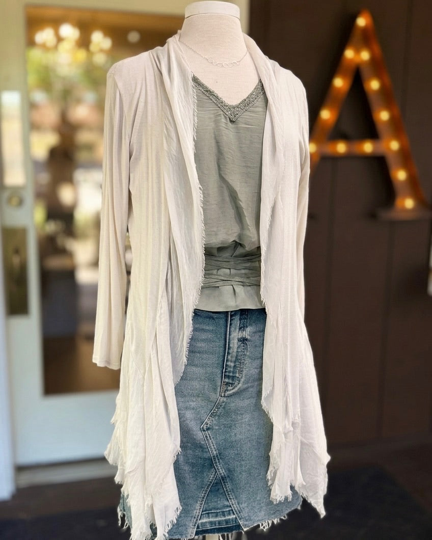 Clara beige silk cardigan on a mannequin, with a draped open front and fringed hem, styled over a green top and denim skirt.