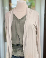 Close-up of the Clara beige silk cardigan's draped neckline and fringed open front, layered over a green V-neck top.