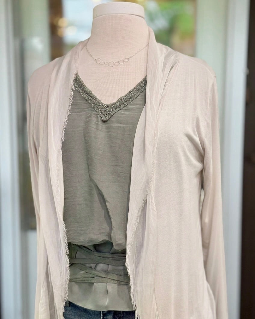 Close-up of the Clara beige silk cardigan's draped neckline and fringed open front, layered over a green V-neck top.