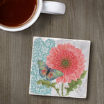 Coaster with floral design featuring a pink flower and butterfly on a wooden surface with a cup of coffee.