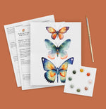 Butterfly illustration sheet with paint swatches and a brush on a brown background