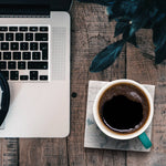 Laptop and coffee cup on a wooden table with a plant