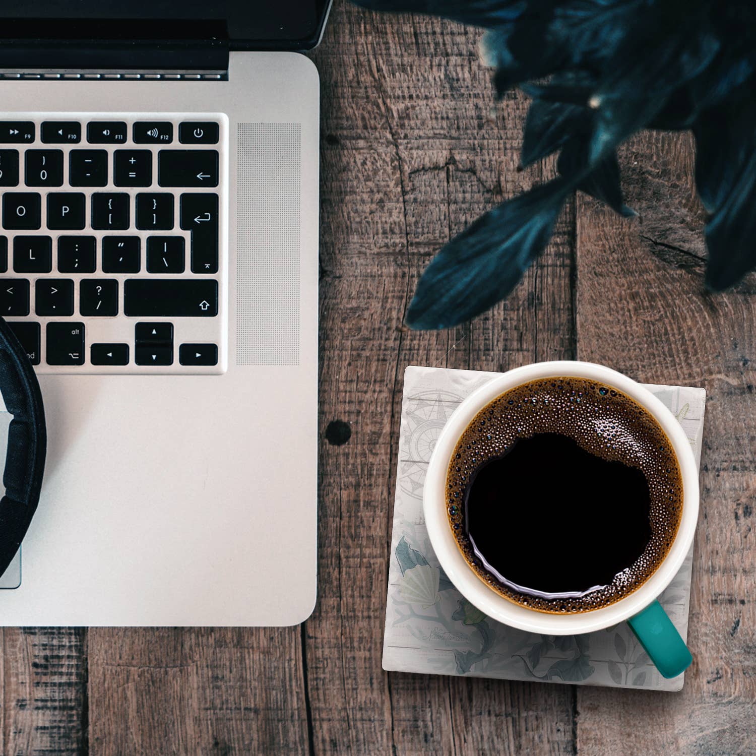 Laptop and coffee cup on a wooden table with a plant