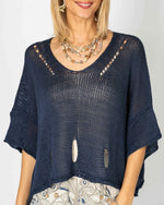 Model wearing the Eleni navy cropped sweater with layered necklaces and patterned bottoms, showing its open knit.