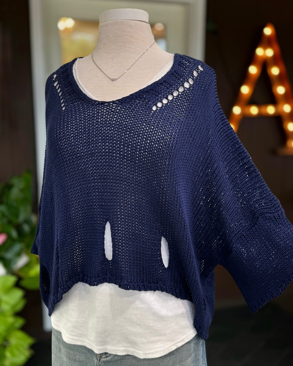 Eleni navy cropped sweater on a mannequin with one sleeve extended to show its wide shape and shoulder cutouts.