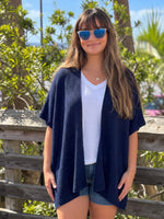 Front view of the Elise Wrap Poncho in Navy worn open over a white top and denim shorts.