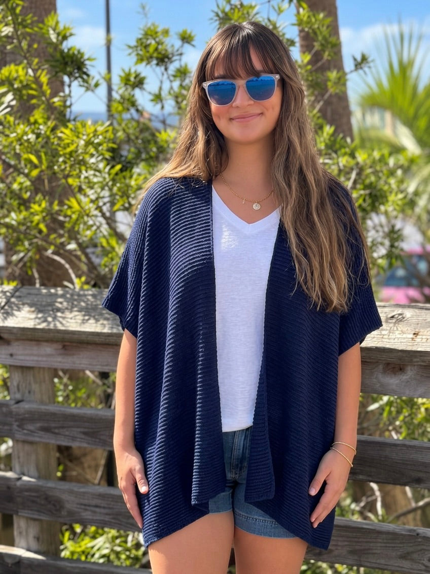 Front view of the Elise Wrap Poncho in Navy worn open over a white top and denim shorts.