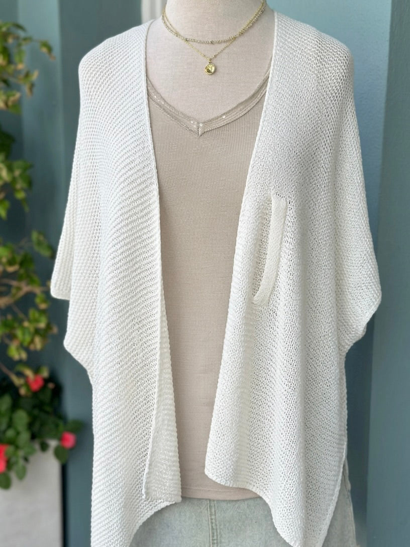 Elise Wrap Poncho in White worn open on a mannequin over a beige top, showing its draped front and open-knit texture.