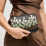 Person holding a floral clutch purse with a plain background