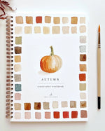 Autumn Watercolor Workbook by Emily Lex Studio featuring a watercolor pumpkin and fall color palette, surrounded by warm autumn hues and art tools.
