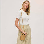 A woman wearing a white short-sleeve polo shirt and beige trousers, carrying a small tan crossbody bag with a matching strap against a light gray studio background.