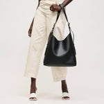 Person holding a black leather handbag against a white background