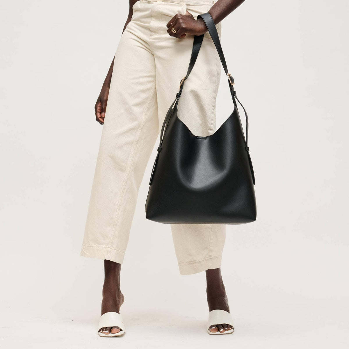 Person holding a black leather handbag against a white background