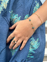 Blue apatite flower bracelet worn beside a gold-tone chain bracelet against blue floral fabric.