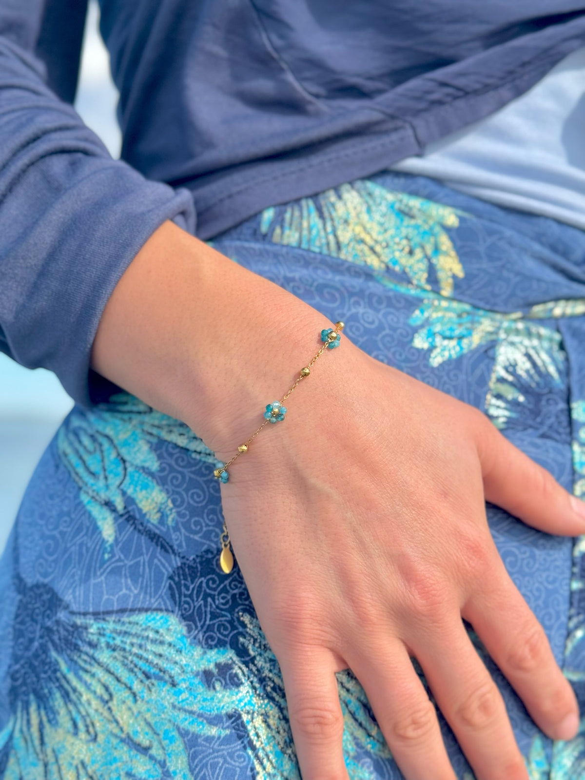 Blue apatite flower bracelet worn alone on the wrist with a navy sleeve and blue floral fabric.