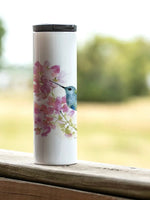 17 oz stainless steel tumbler with hummingbird and floral artwork, shown outdoors from Ardor Boutique