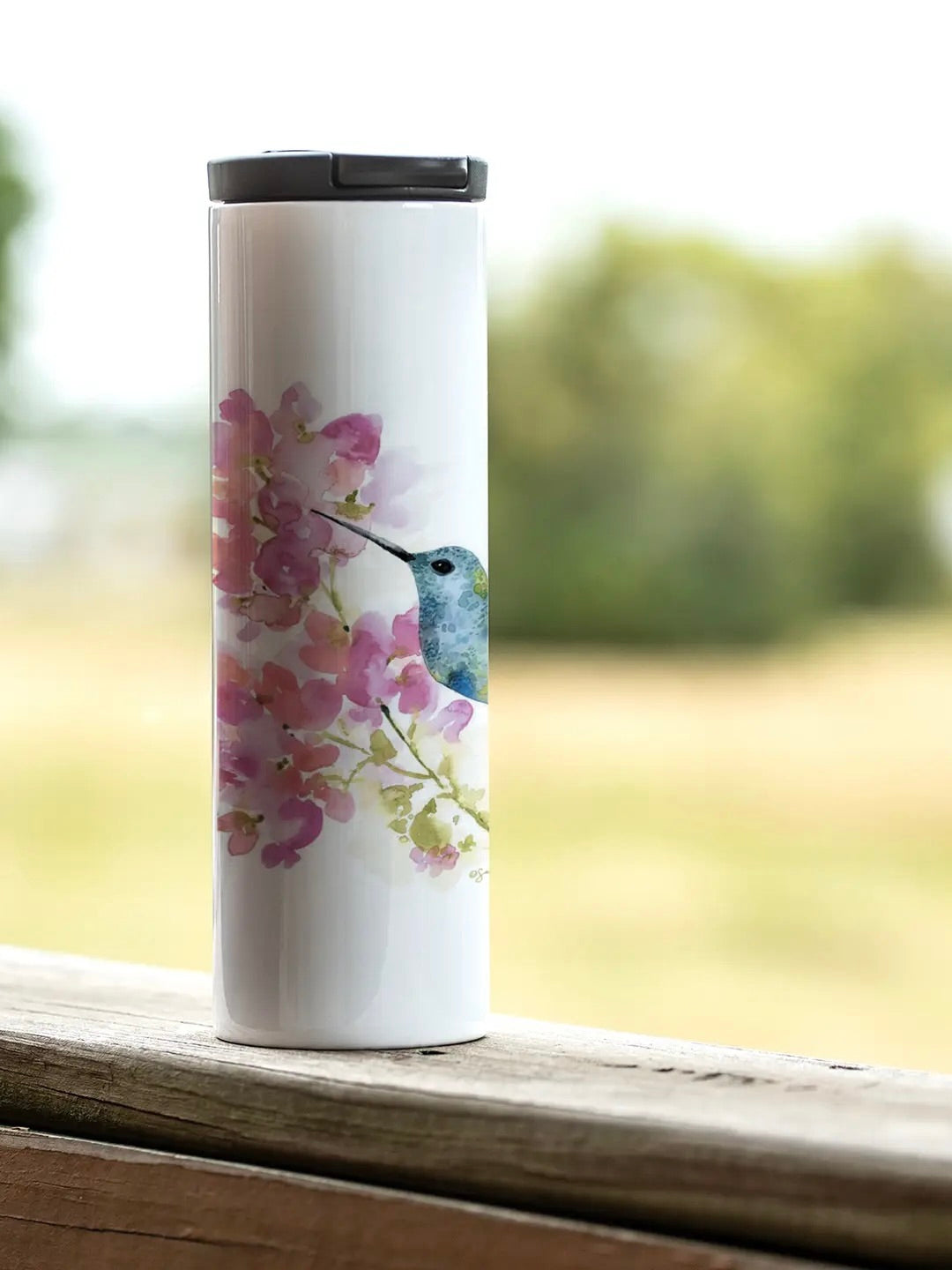 17 oz stainless steel tumbler with hummingbird and floral artwork, shown outdoors from Ardor Boutique