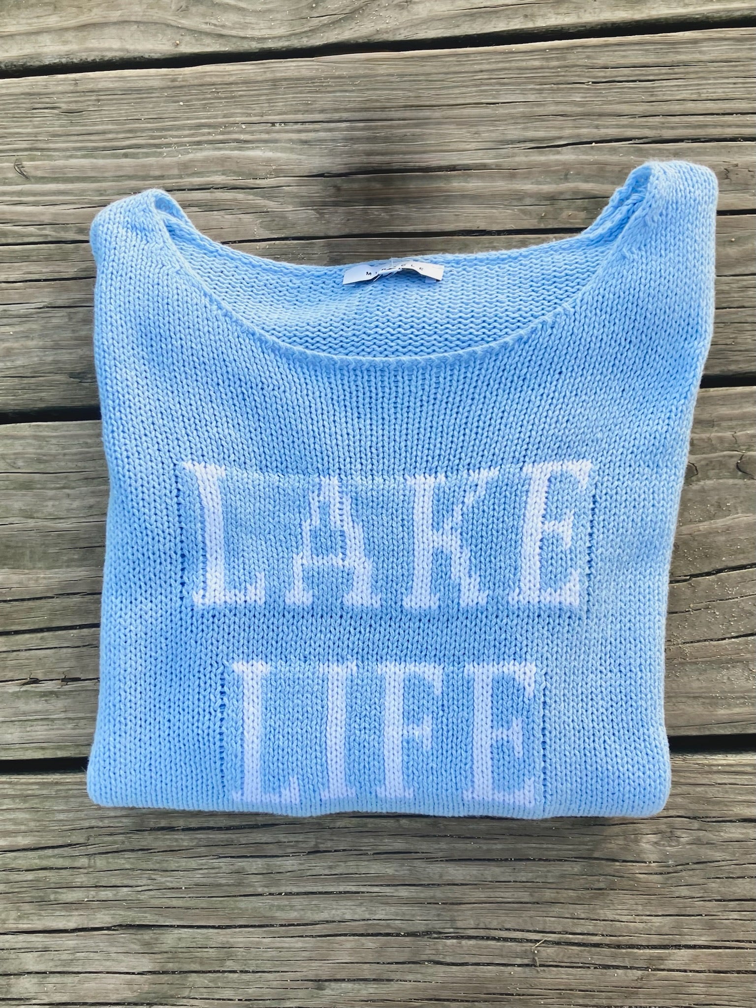 Cotton acrylic sky blue Lake Life sweater folded on wooden dock from Ardor Boutique