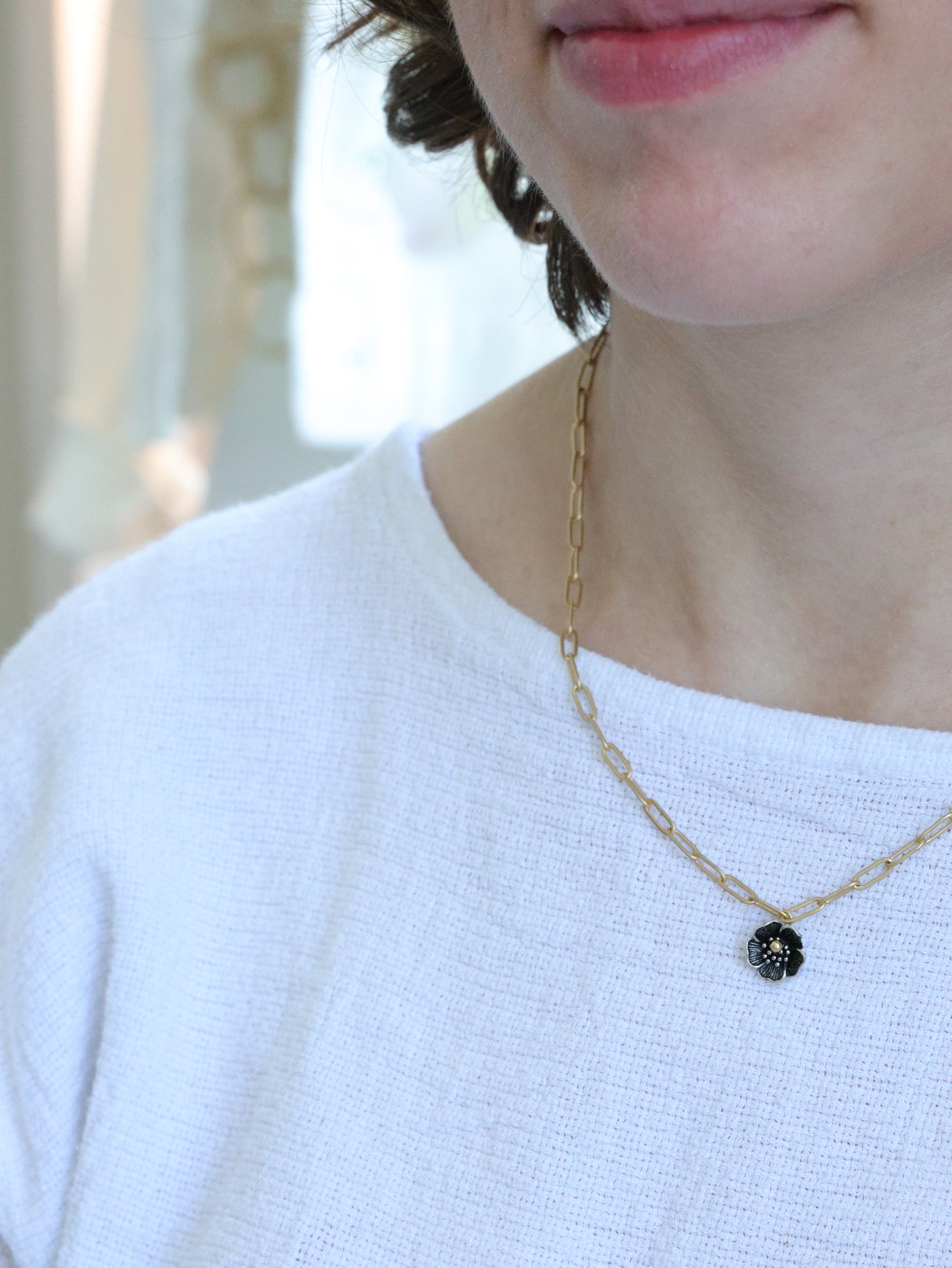 Close-up of a woman wearing a matte gold necklace with a small five-petal flower pendant – minimalist floral jewelry by Ardor Boutique