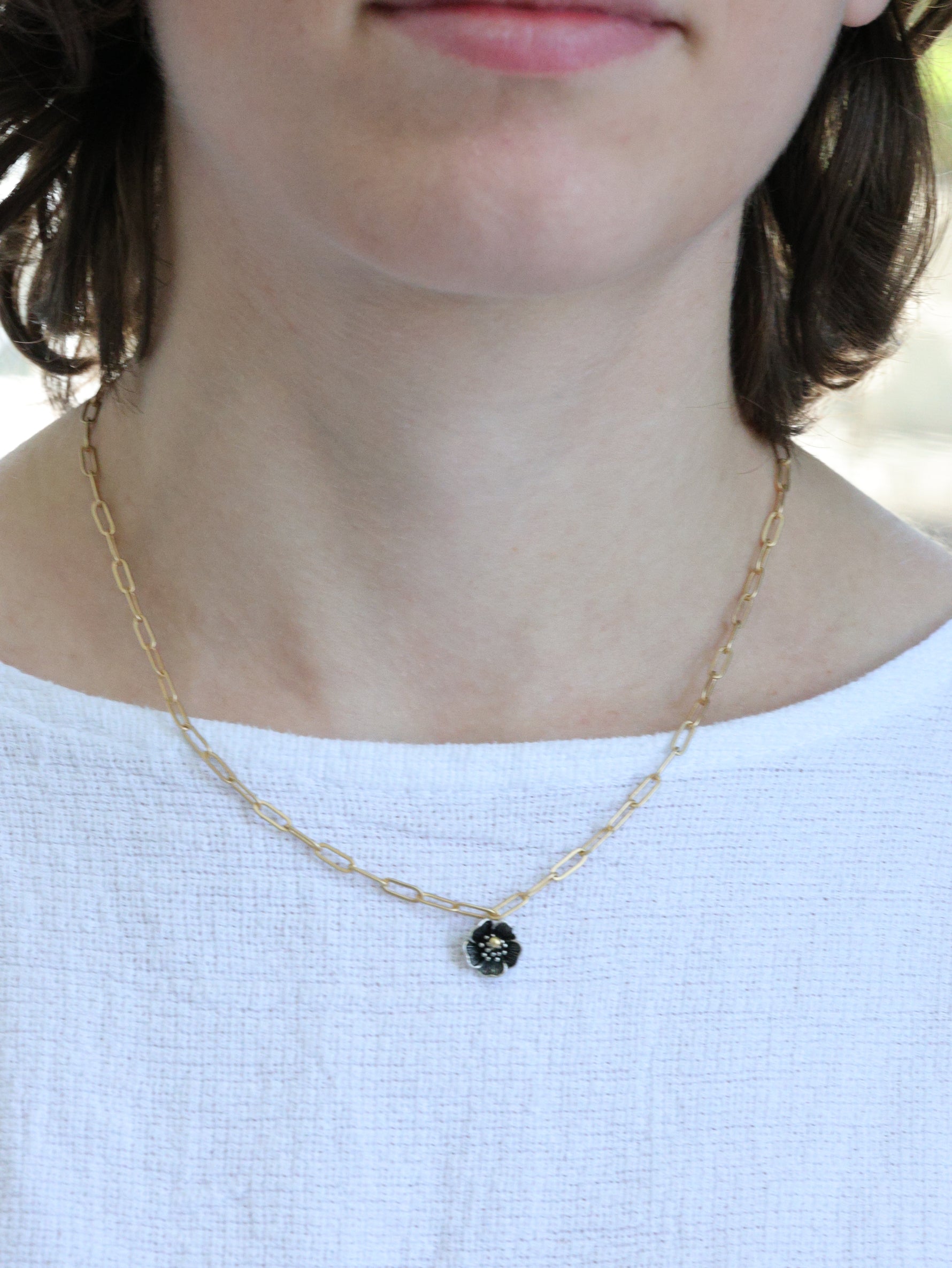 Close-up of a woman wearing a matte gold necklace with a small five-petal flower pendant – minimalist floral jewelry by Ardor Boutique
