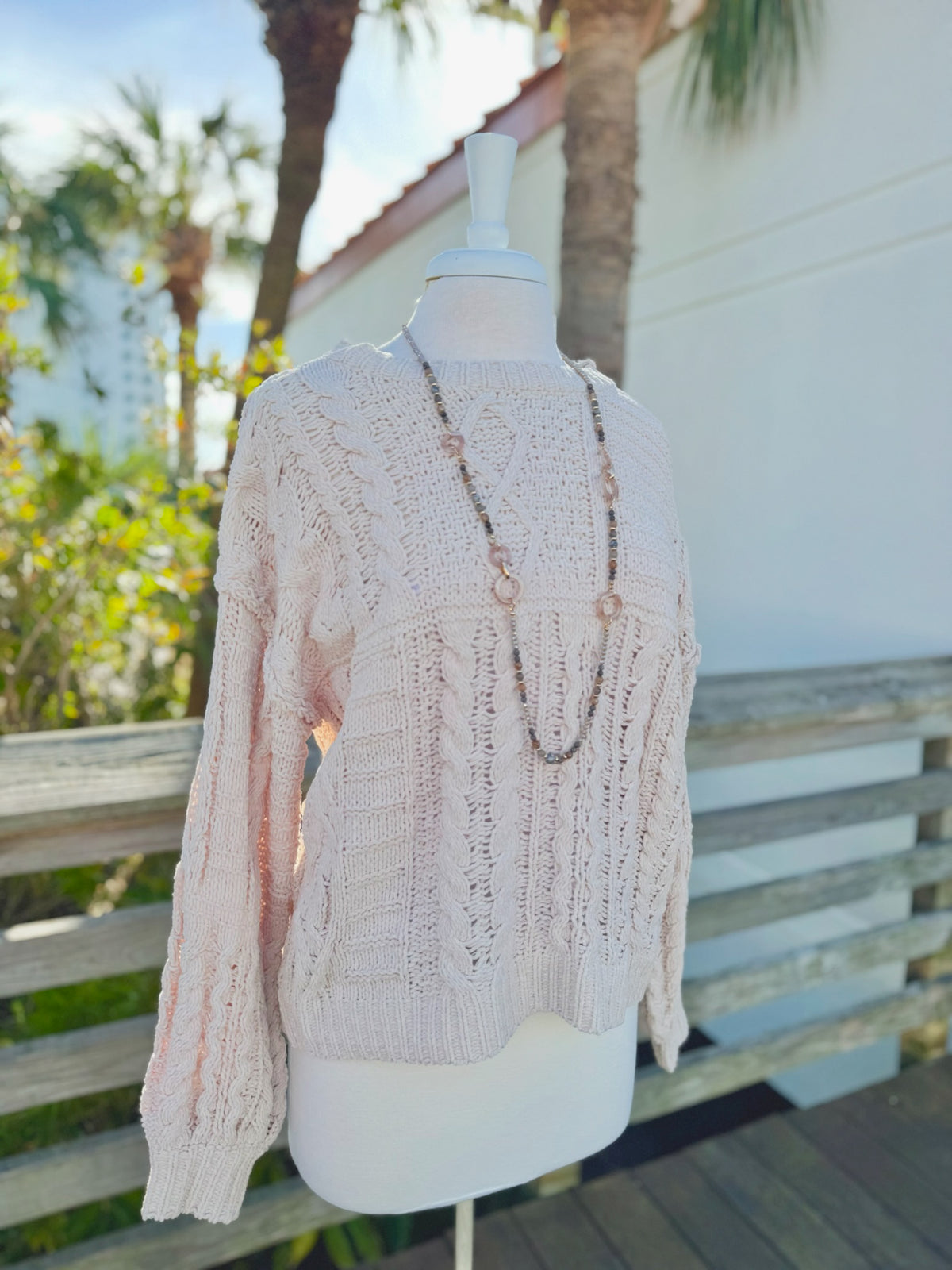 Side view Cable knit sweater in beige on a mannequin outdoors with a long taupe necklace