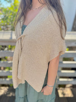 Person wearing a gold knitted shrug over a light green dress outdoors.