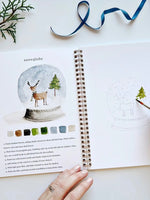 Winter Watercolor Workbook open to snowglobe painting page with step-by-step instructions, color palette, and outline sketch by Emily Lex